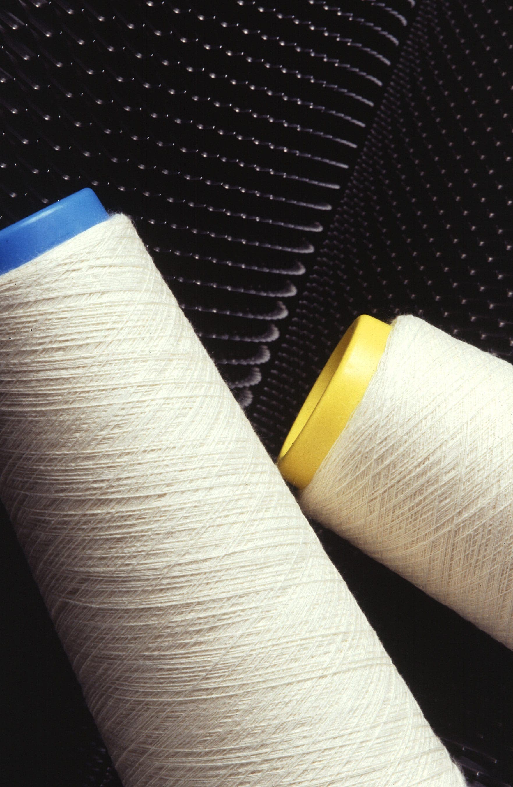 Two cones of undyed white yarn on a dark textured surface
